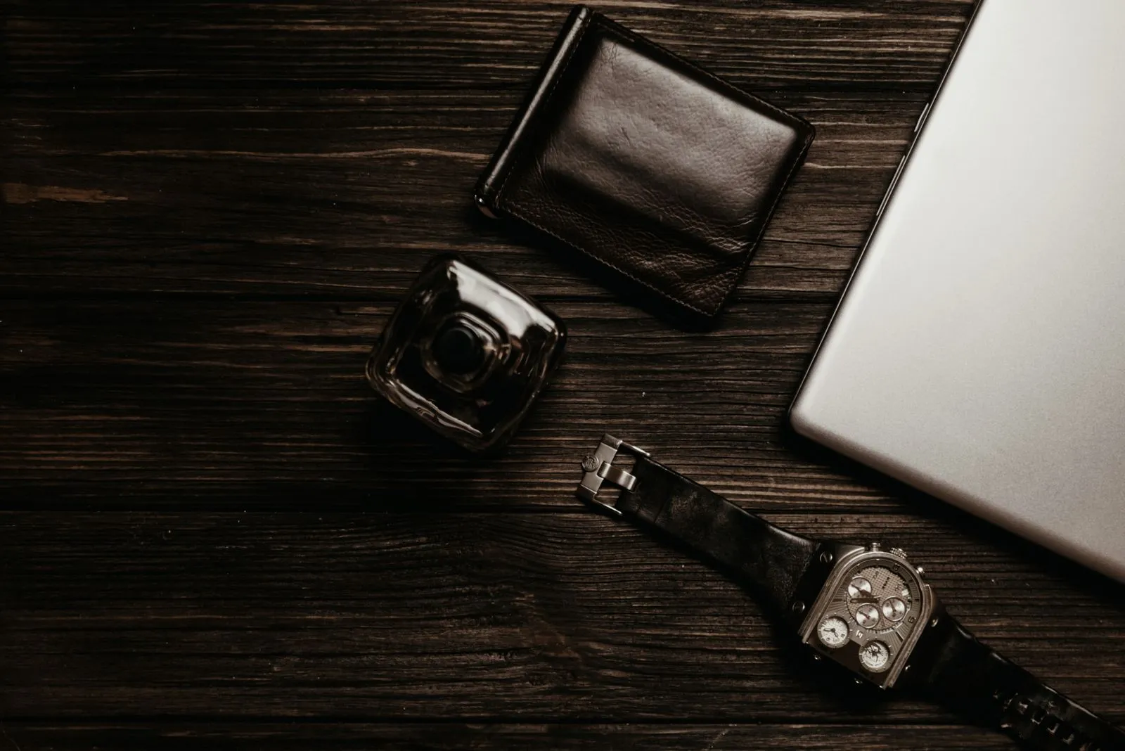 Leather wallet, glass perfume bottle and watch on dark wood